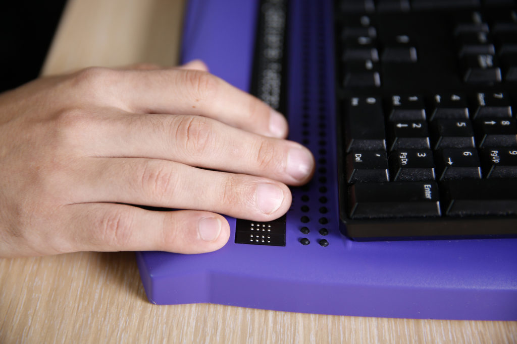 Blind person's hand using computer with braille computer display and a computer keyboard. 